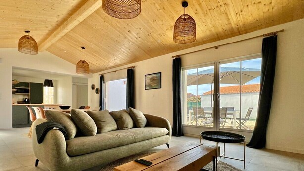 Una sala de estar moderna con un sofá, una mesa de centro de madera y vistas al exterior a través de amplios ventanales.