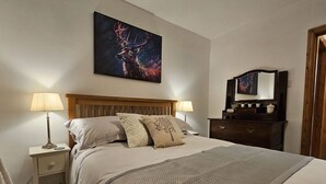 A neatly made bed with a headboard, two bedside lamps, a nightstand, and a dresser with a mirror.