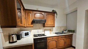 A kitchen with wooden cabinets, a gas stove, a microwave, and a kettle.