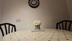 A dining table with a polka dot tablecloth, two chairs, a vase with flowers, and a wall clock.