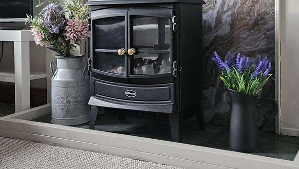 A black wood-burning stove with glass doors, positioned in front of a marble fireplace.