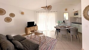 A modern living room with a sofa, a dining table, and a kitchen area with cabinets and a microwave. - Mini Villa near Pinarello beach (Zonza)