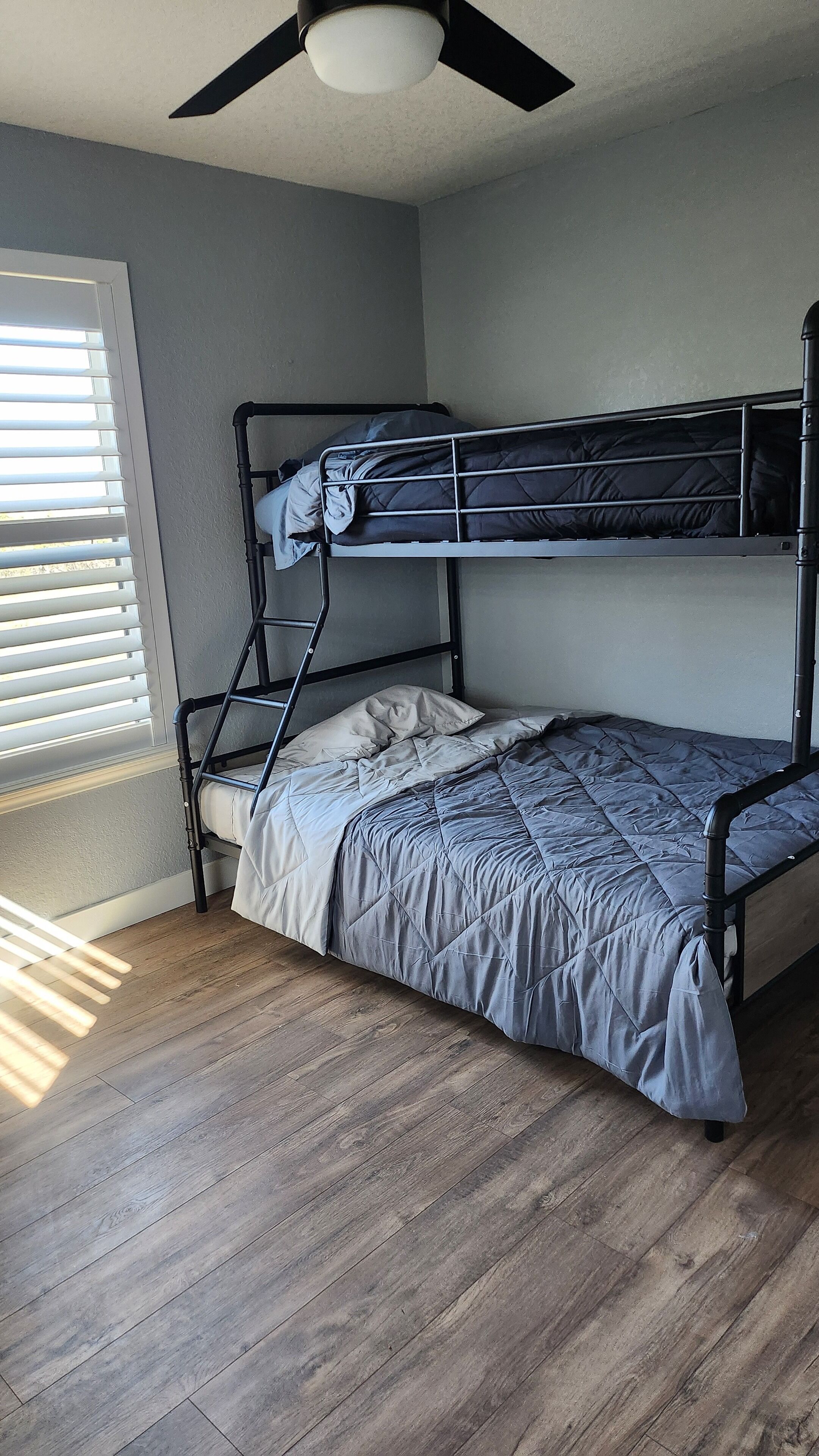 A bunk bed with a ladder, a ceiling fan, and a window with blinds.