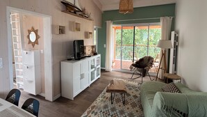 A spacious living area with a wooden ceiling, a sailboat decoration, a television on a cabinet, a rocking chair, and a view through a glass door to an outdoor balcony. - Cosy, comfortable 4-star apartment (Vaux-sur-Mer)