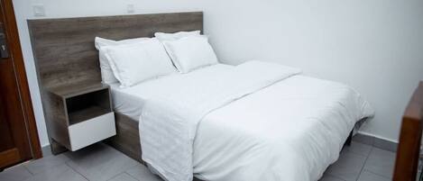A neatly made bed with white bedding and a wooden headboard.
