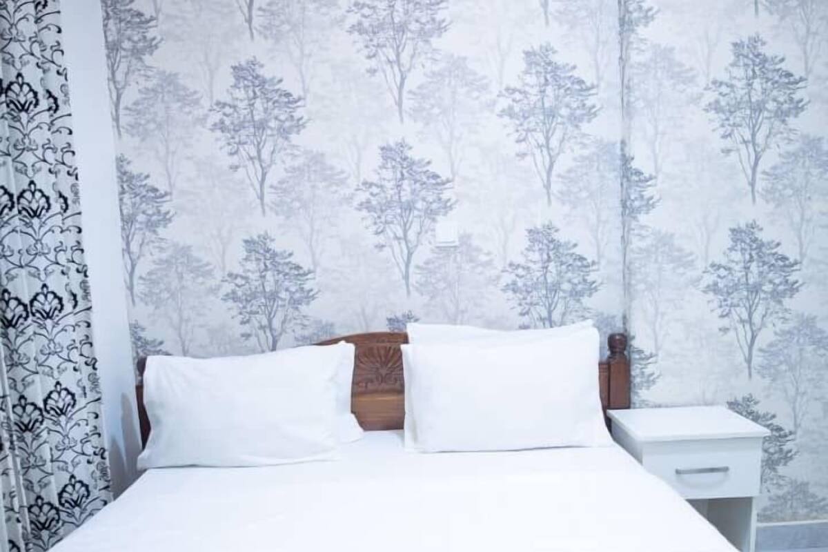 A neatly made bed with white linens, a wooden headboard, and a nightstand with a white lamp.