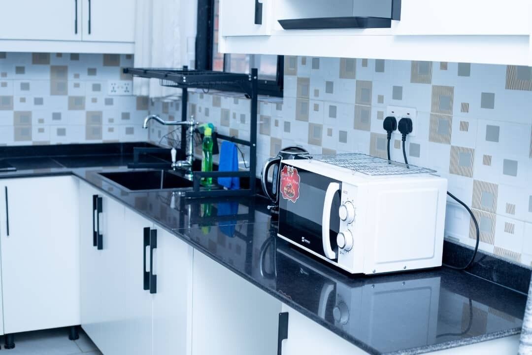 A modern kitchen with white cabinets, a black countertop, and a white microwave.