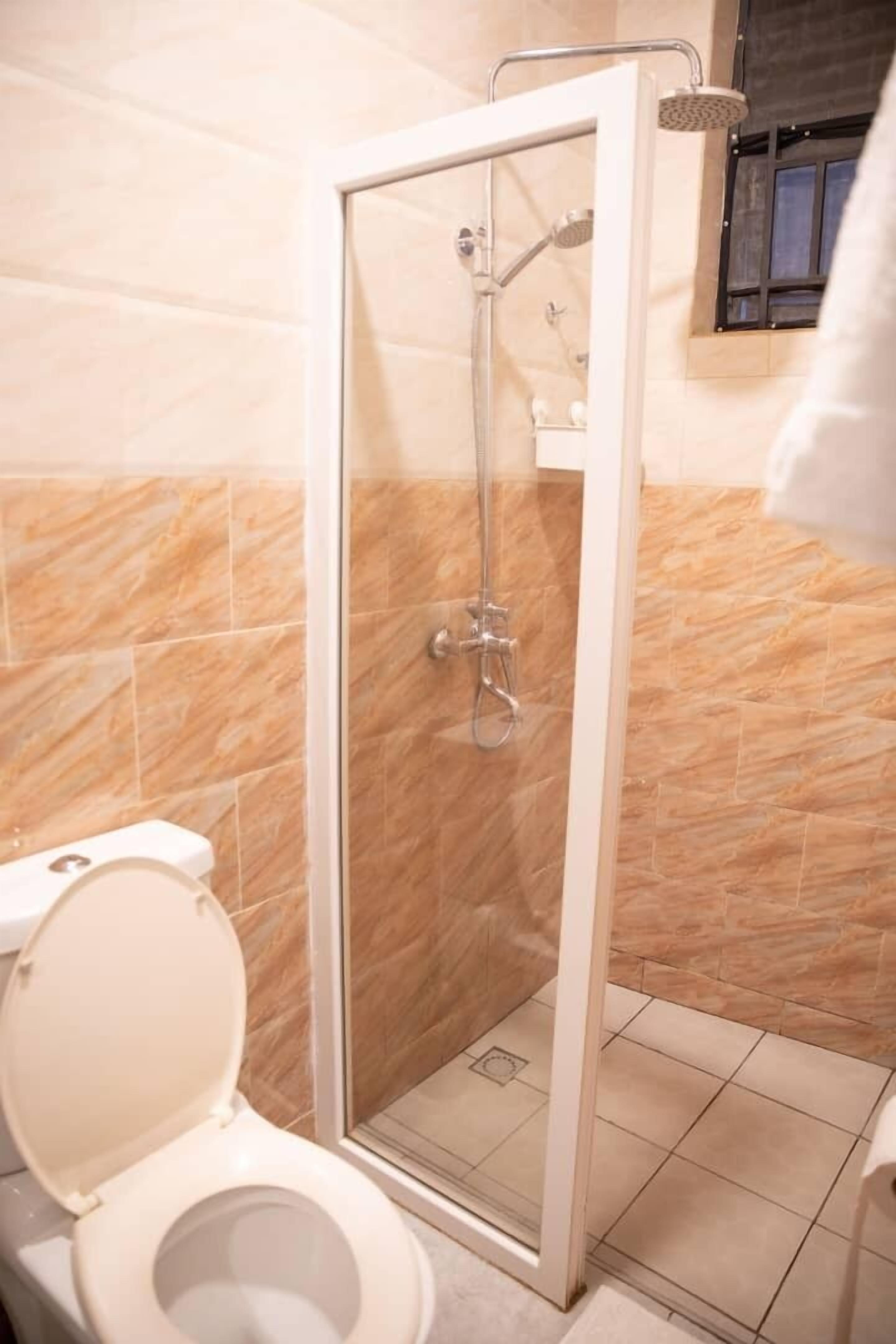 Une salle de bain avec une douche à parois de verre, des toilettes et des murs recouverts de carreaux beiges.