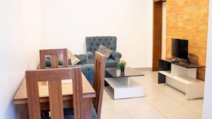 Un salon moderne avec une table à manger, des chaises, un canapé et un téléviseur, le tout placé devant un mur en briques.