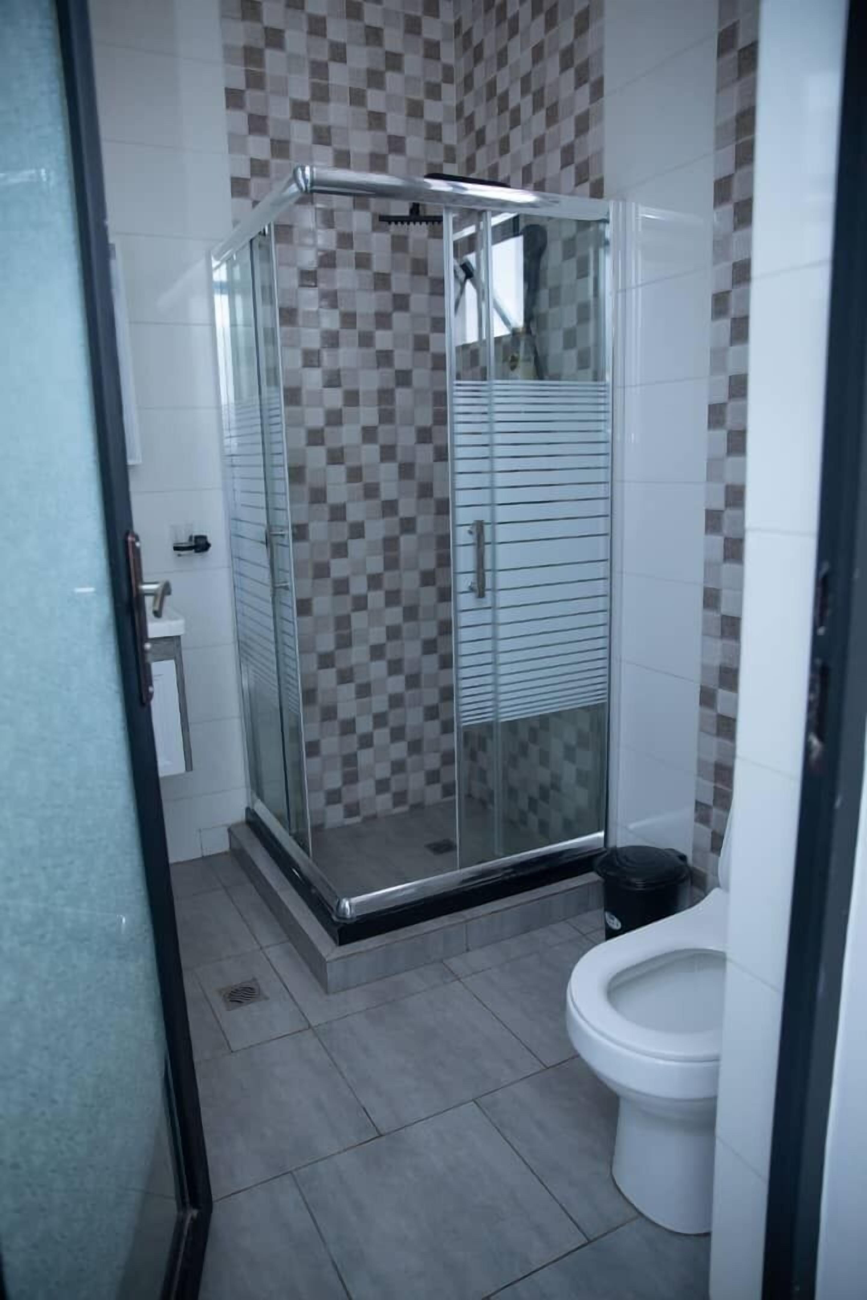 A bathroom with a glass-enclosed shower, a toilet, and a checkered tile wall.