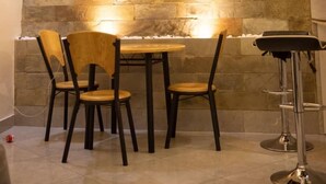 Un coin repas avec un mur en pierre, une table ronde, quatre chaises en bois et un tabouret de bar.
