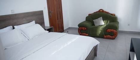A bedroom with a large bed, a wooden headboard, a green armchair with a pillow, and a wooden door.