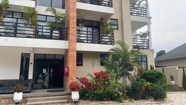 Un hôtel à plusieurs étages doté de balcons, d’une façade en briques et d’une entrée aménagée avec des plantes et des fleurs en pot.