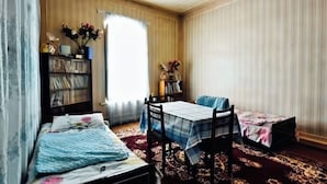 Una habitación con una cama, una pequeña mesa con sillas, una estantería y una ventana con cortinas.
