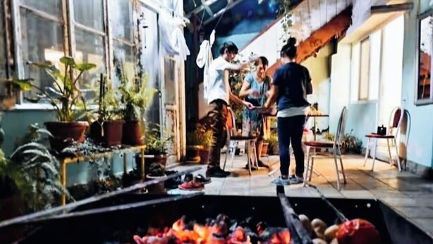 Un espacio al aire libre rústico con un brasero, plantas en macetas y una mesa de madera.