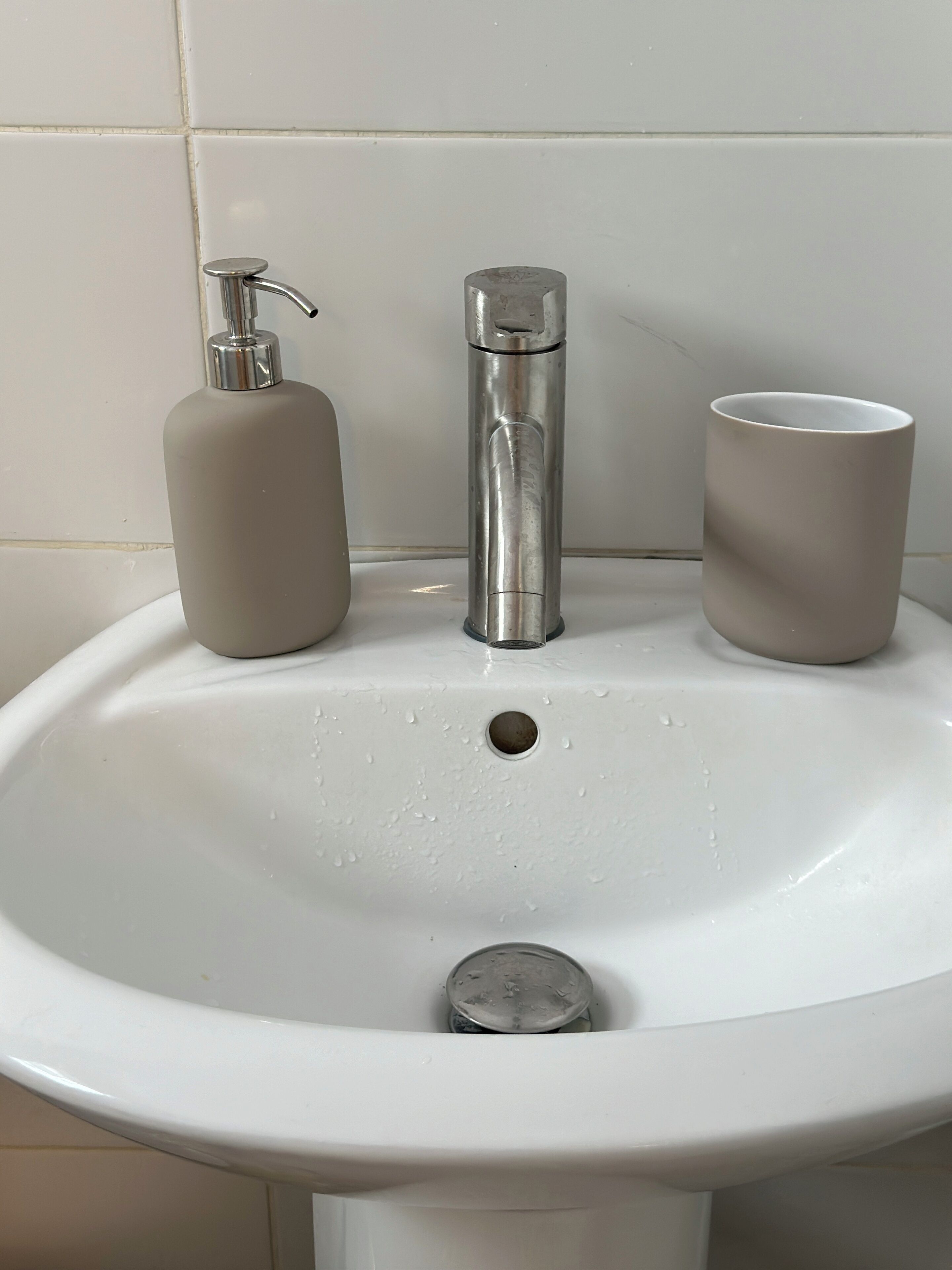 A bathroom sink with a faucet, a soap dispenser, and a cup.