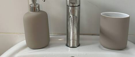A bathroom sink with a faucet, a soap dispenser, and a cup.