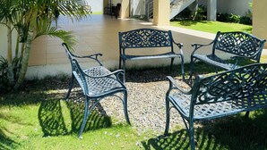 A covered outdoor seating area with metal benches and a palm tree.
