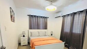 A bedroom with a bed, two bedside tables, a ceiling fan, and curtains.