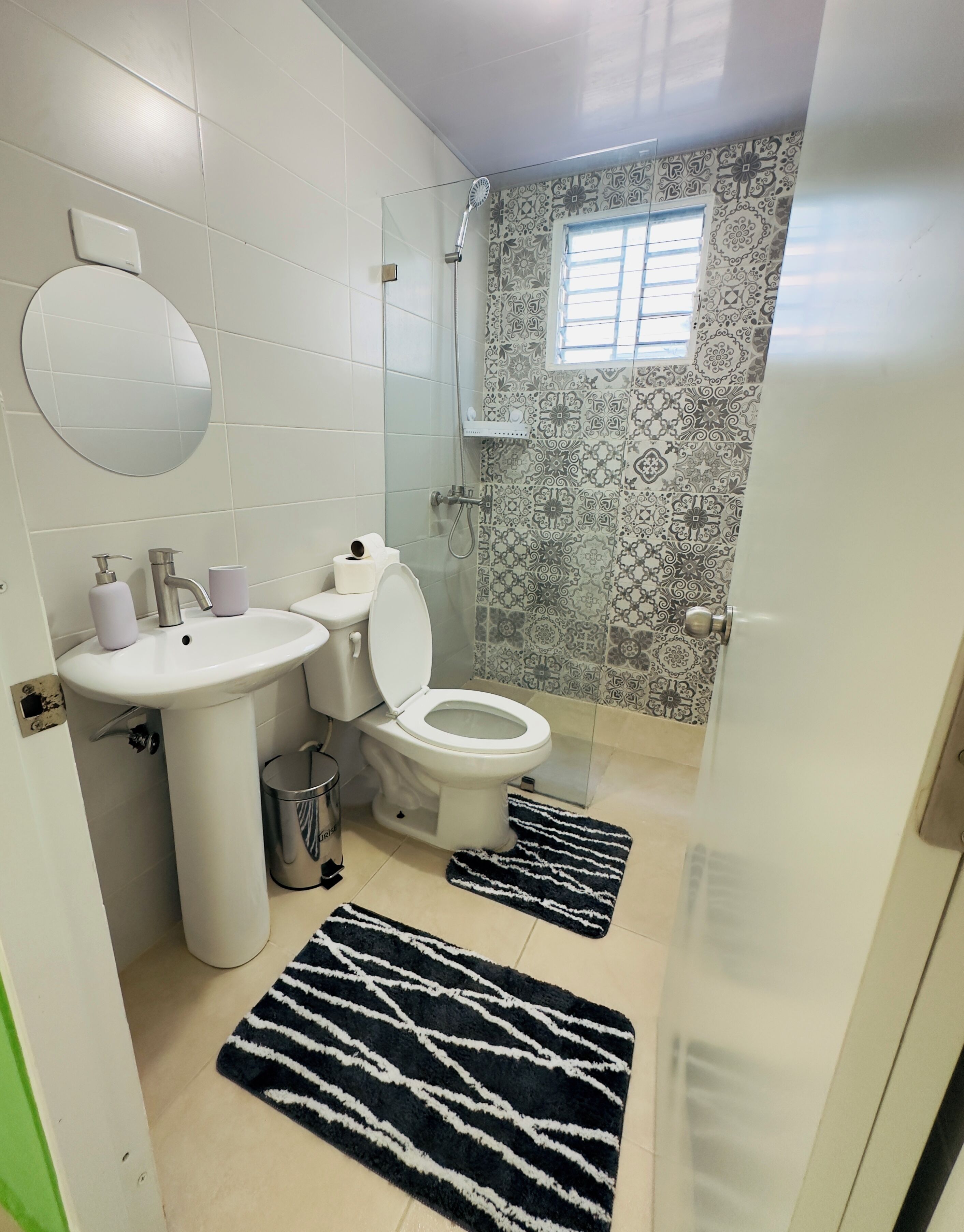 Een badkamer met toilet, wastafel en douche. Er liggen twee vloerkleden op de vloer.