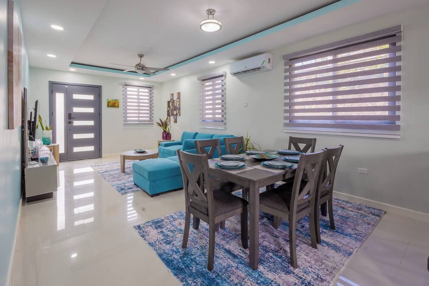 Una sala de estar moderna con comedor, que incluye un sofá azul, una mesa de comedor de madera y un ventilador de techo.