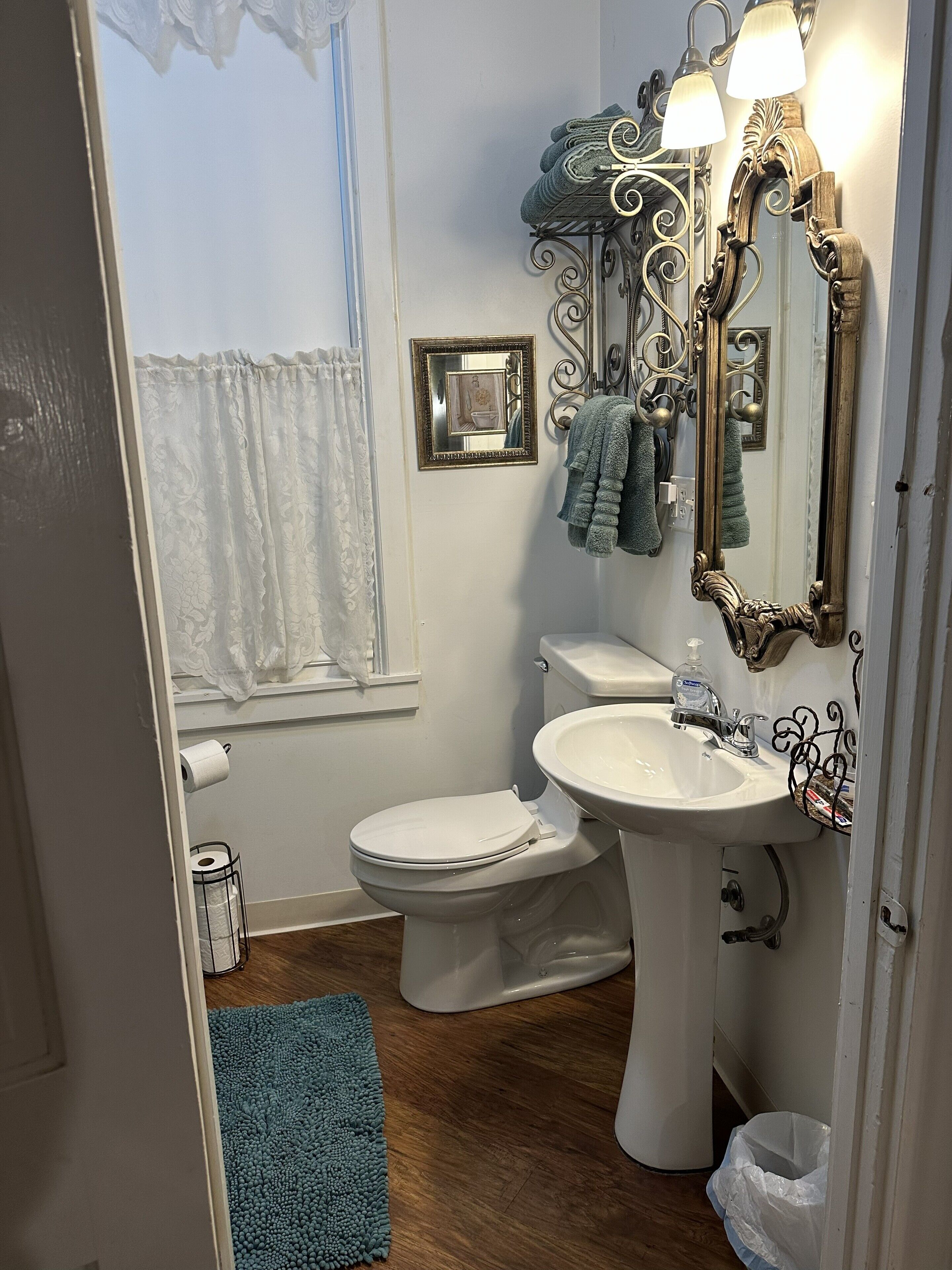 A bathroom with a toilet, sink, decorative mirror, and towel rack.
