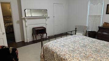 Une chambre à coucher comprenant un lit, une commode, une table de chevet, un miroir, une cheminée et une porte donnant sur une autre pièce.