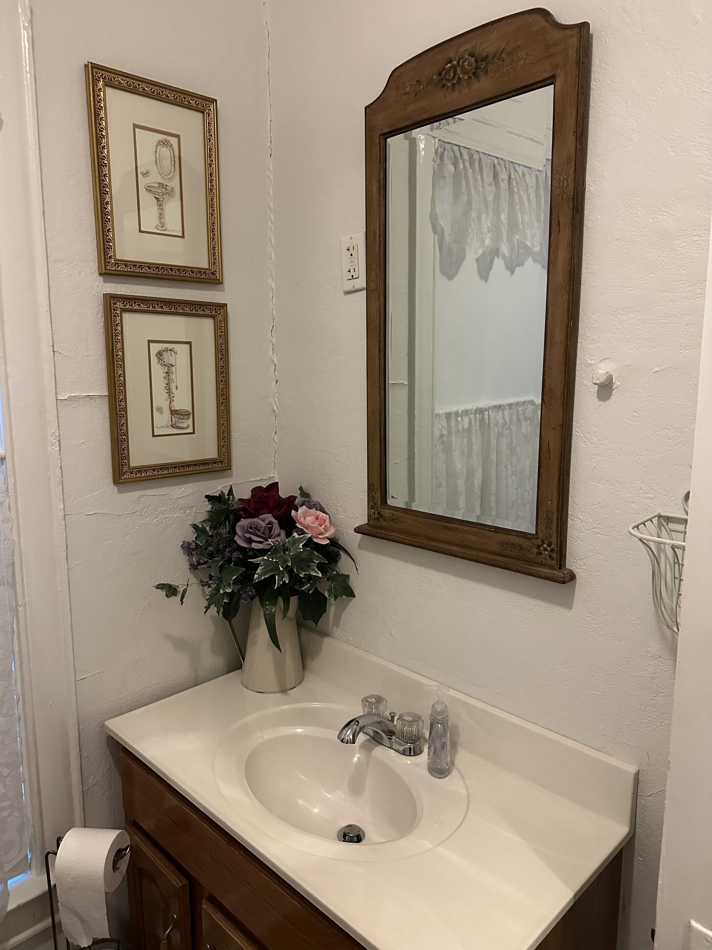 Een badkamer met een wastafel, spiegel, lijstjes met foto's en een bloemenvaas.