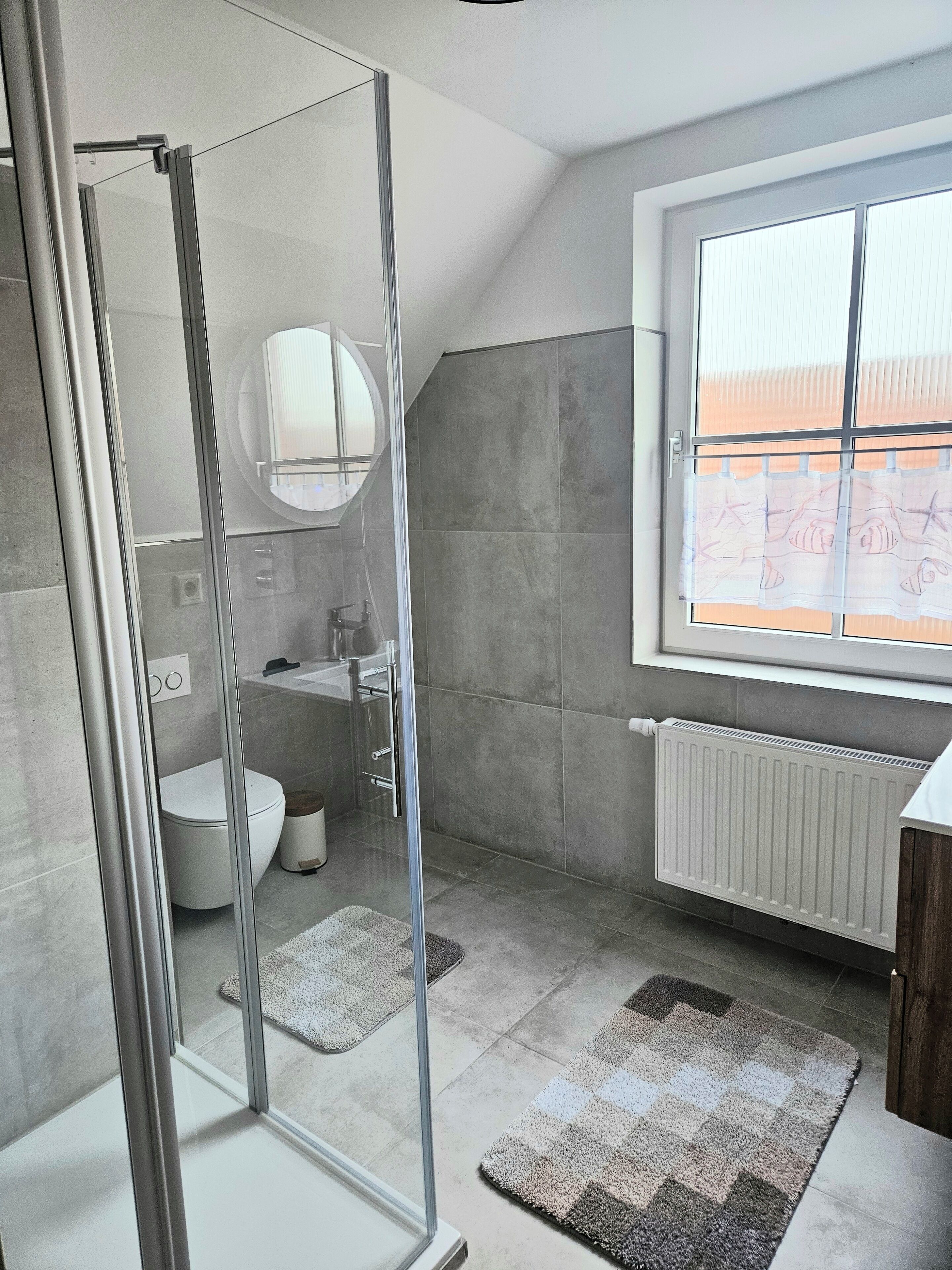 Une salle de bain moderne avec une douche à parois de verre, des toilettes, un lavabo et une fenêtre donnant sur un beau paysage.