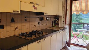 Una cocina con armarios blancos, encimera negra y estufa a gas. Se observa una ventana con vistas a un balcón con sillas.