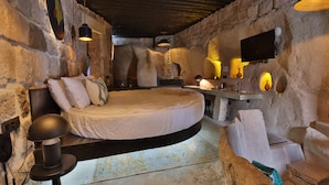 A rustic stone room with a bed, a desk, and a television mounted on the wall. - EKA CAVE MAISON (Ürgüp)