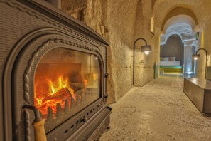 Un interno con pareti in pietra, un camino a legna, una panca e un vialetto che conduce alla zona notte.