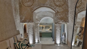 A modern interior with a stone-textured wall, a central archway leading to a bathroom, and a sofa with patterned cushions. - EKA CAVE MAISON (Ürgüp)