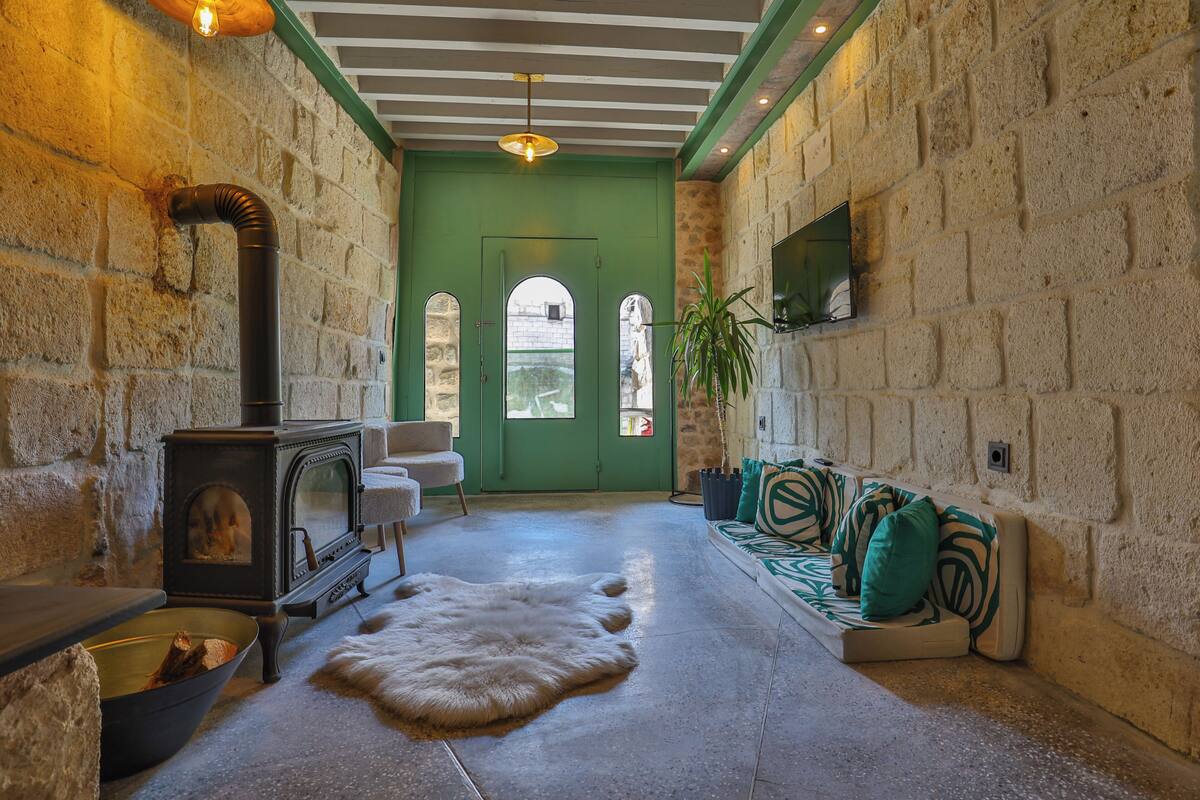 Ein gemütliches Interieur mit einer Steinwand, einer grünen Tür, einem Kamin und einer Sitzecke mit Kissen.