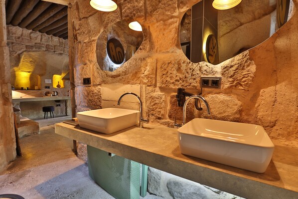 A rustic bathroom with two sinks, stone walls, and a large mirror. - EKA CAVE MAISON (Ürgüp)