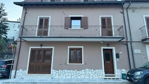 Ein zweistöckiges Gebäude mit Balkon, Steinunterbau und einem Schild, das es als Wohnhaus kennzeichnet.