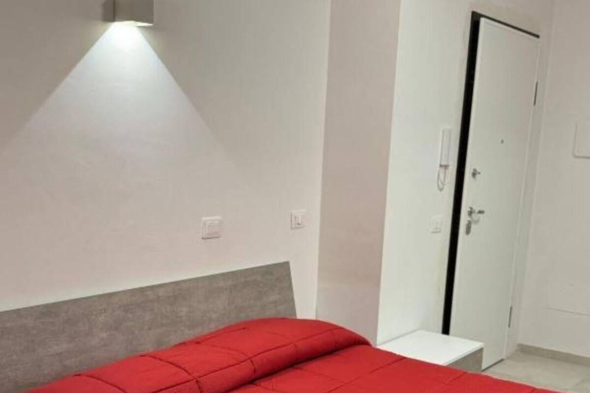Un dormitorio con cama, mesita de noche, luz en la pared y una puerta.