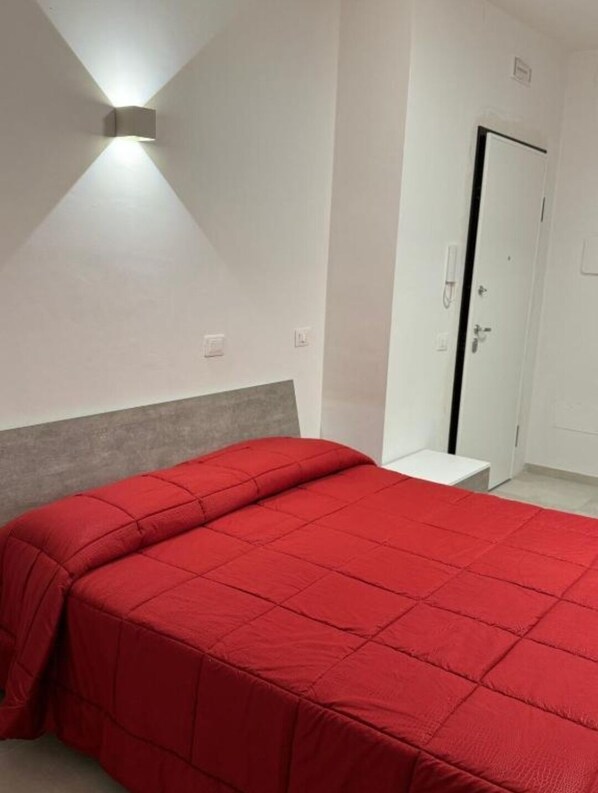 A bedroom with a bed, a nightstand, a wall-mounted light, and a door. - Guest House IN PIAZZETTA (Ateleta)
