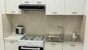 Eine kleine Küche mit weißen Schränken, einem Gasherd, einem Backofen, einer Spüle und einem kleinen Hocker.