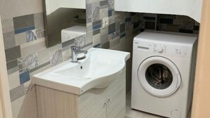 Ein kleines Badezimmer mit Waschbecken, Spiegel und Waschmaschine.
