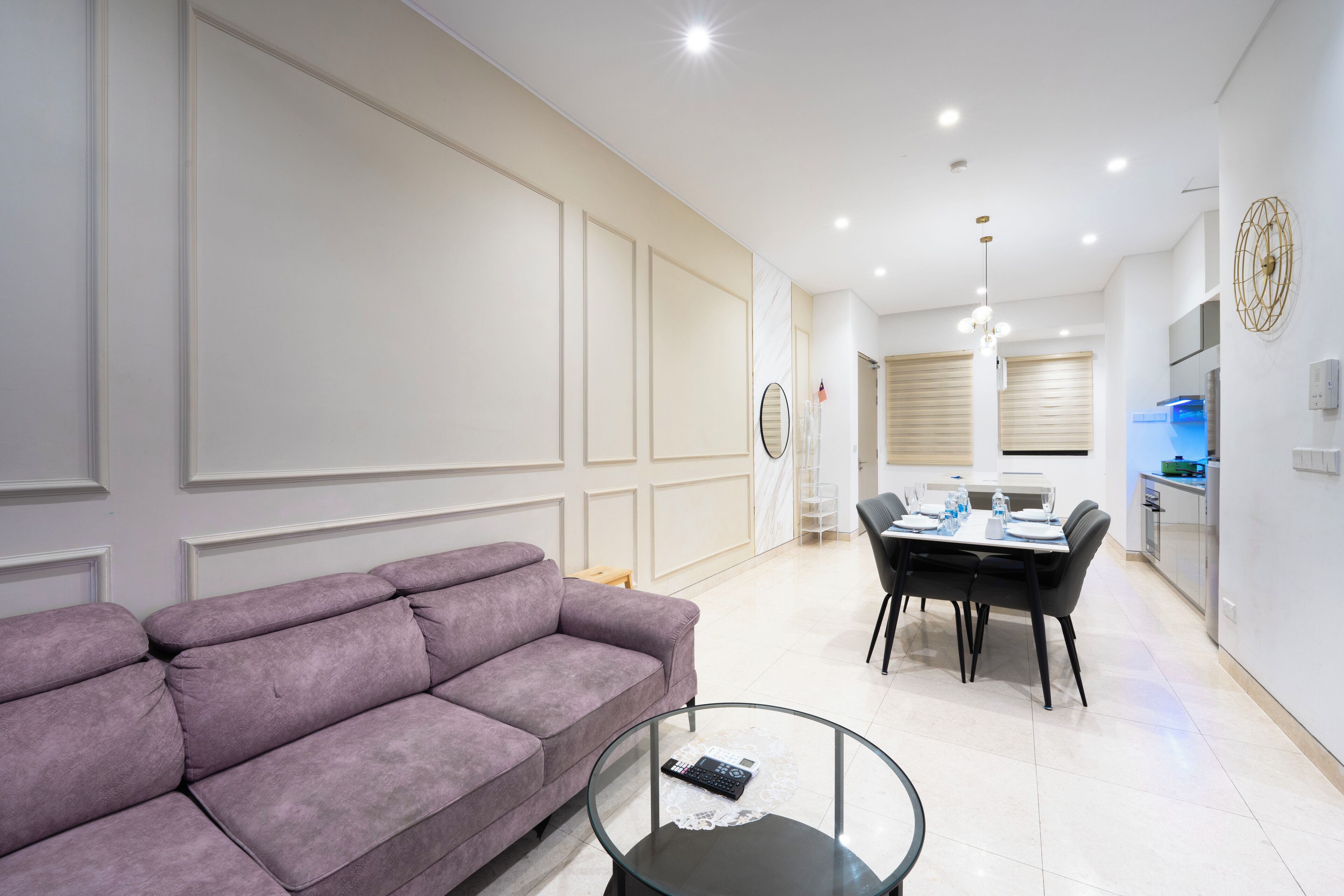 Una sala moderna con un sofá morado, una mesa de centro de vidrio y un comedor con una mesa y sillas.