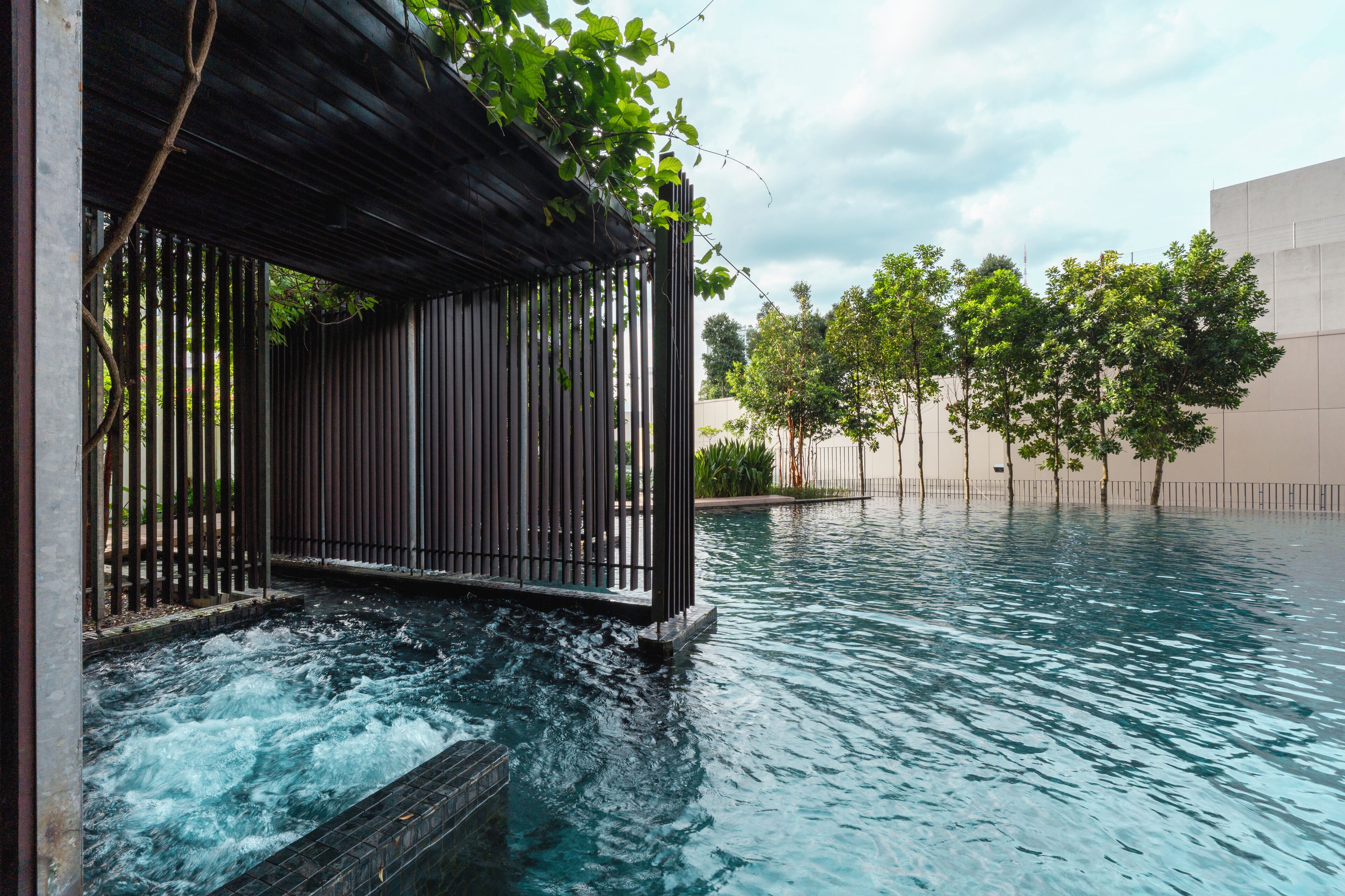 Una piscina con cascata, circondata da alberi e un edificio moderno.