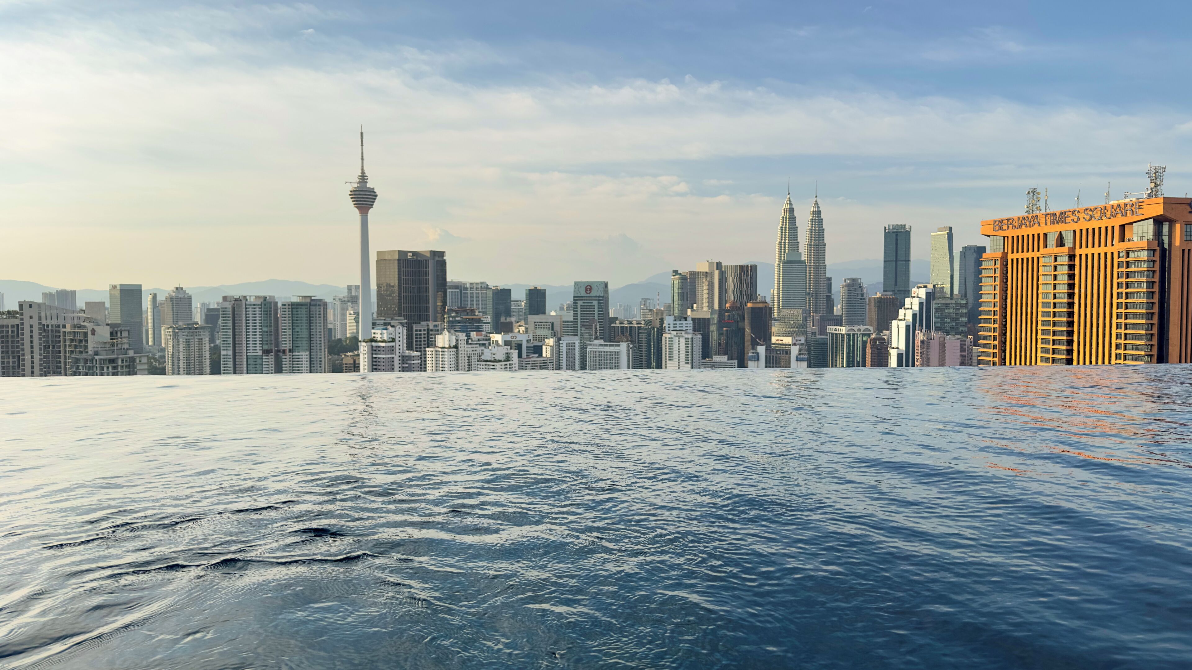 A waterfront cityscape with modern skyscrapers, including a prominent tower and a building labeled "BERJAYA TIMES SQUARE".