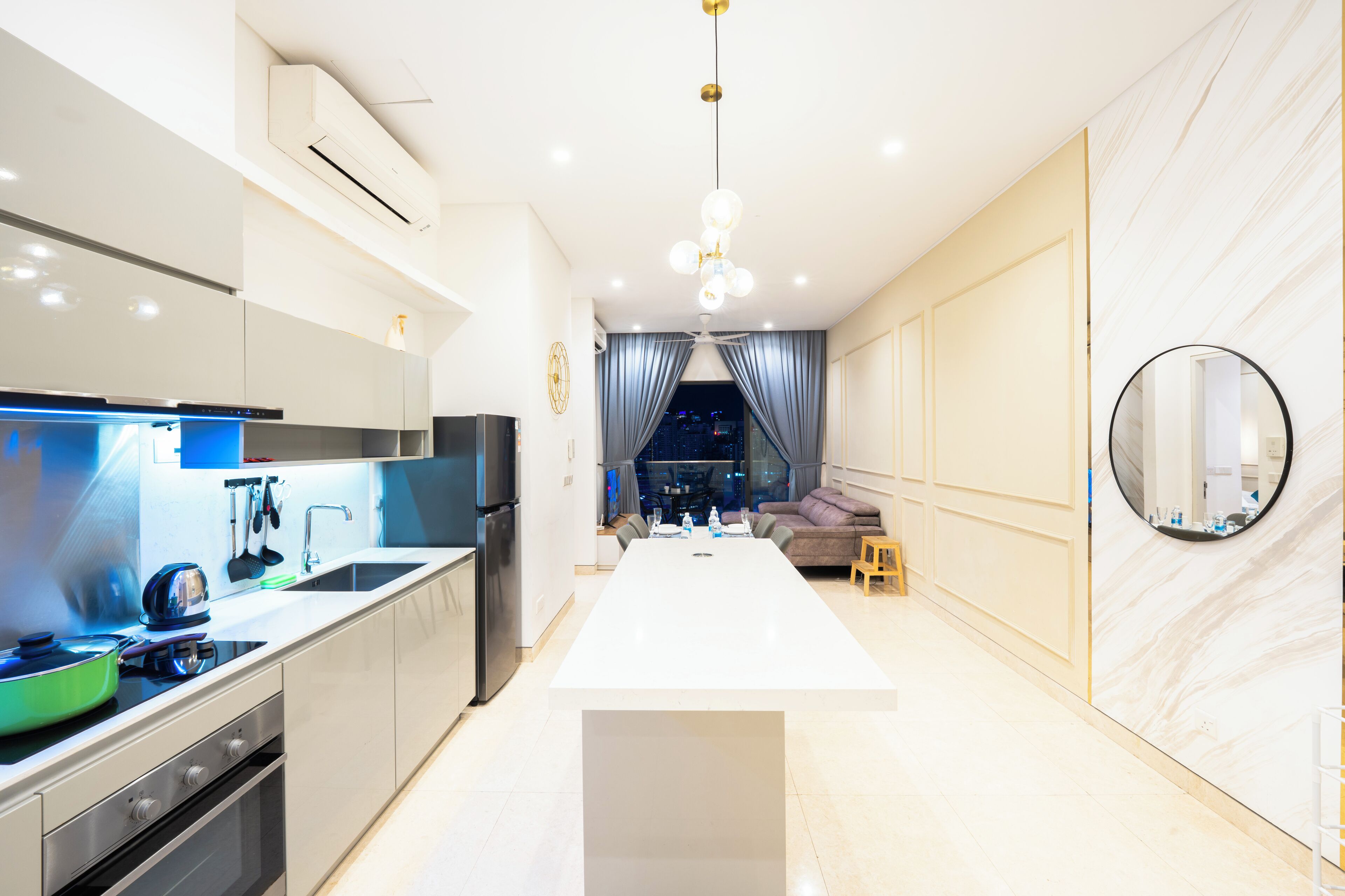 A modern kitchen with a central island, built-in appliances, and a dining area with a sofa and a round mirror.