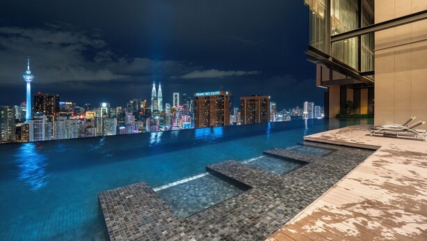 Een dakterras zwembad met een uitzicht op de skyline, inclusief de Petronas Towers, en een modern gebouw met een glazen gevel.