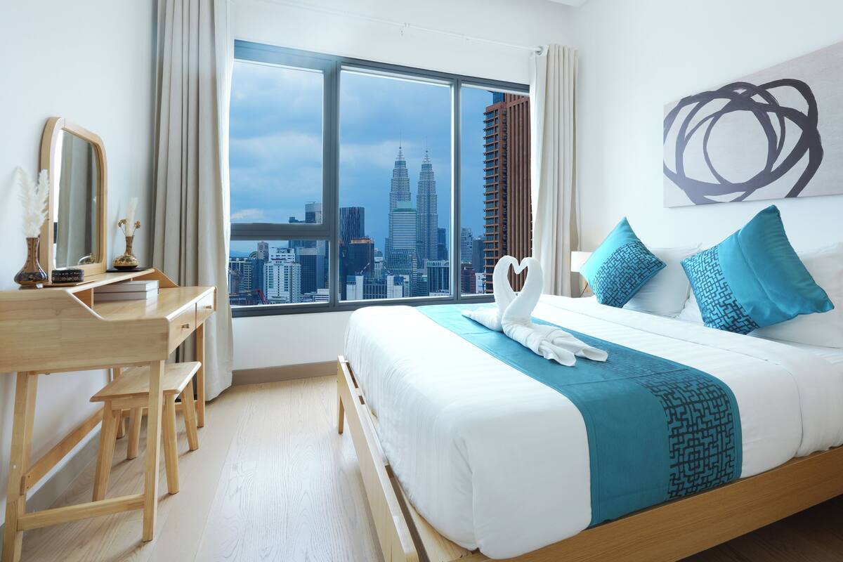 A hotel room with a large bed, a desk, a chair, and a view of the cityscape.