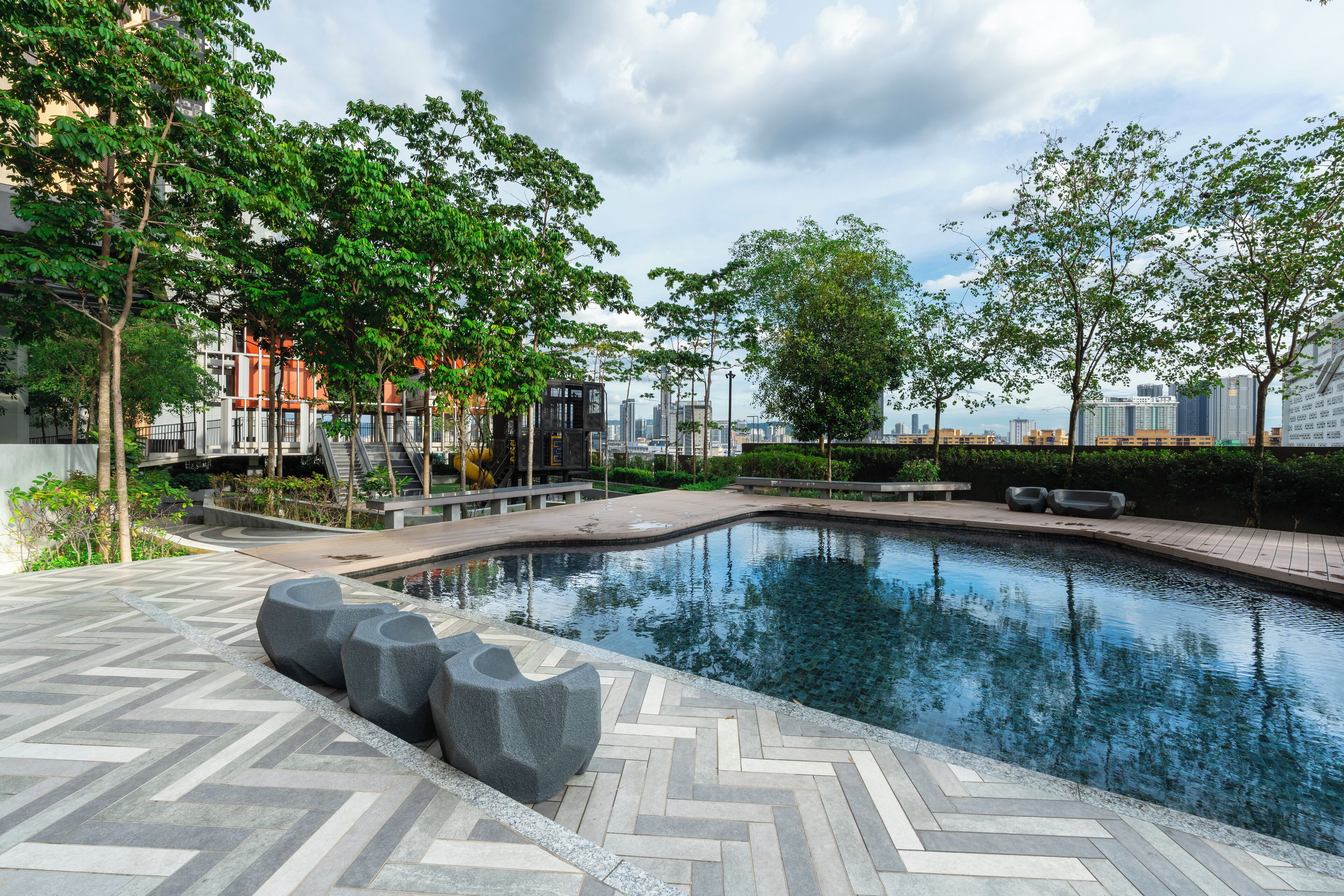 A modern outdoor pool area with a herringbone tile pattern, surrounded by trees and a cityscape in the background.