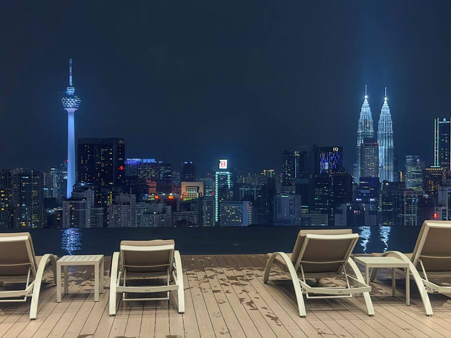 A rooftop lounge with four lounge chairs and a table, overlooking a city skyline at night.
