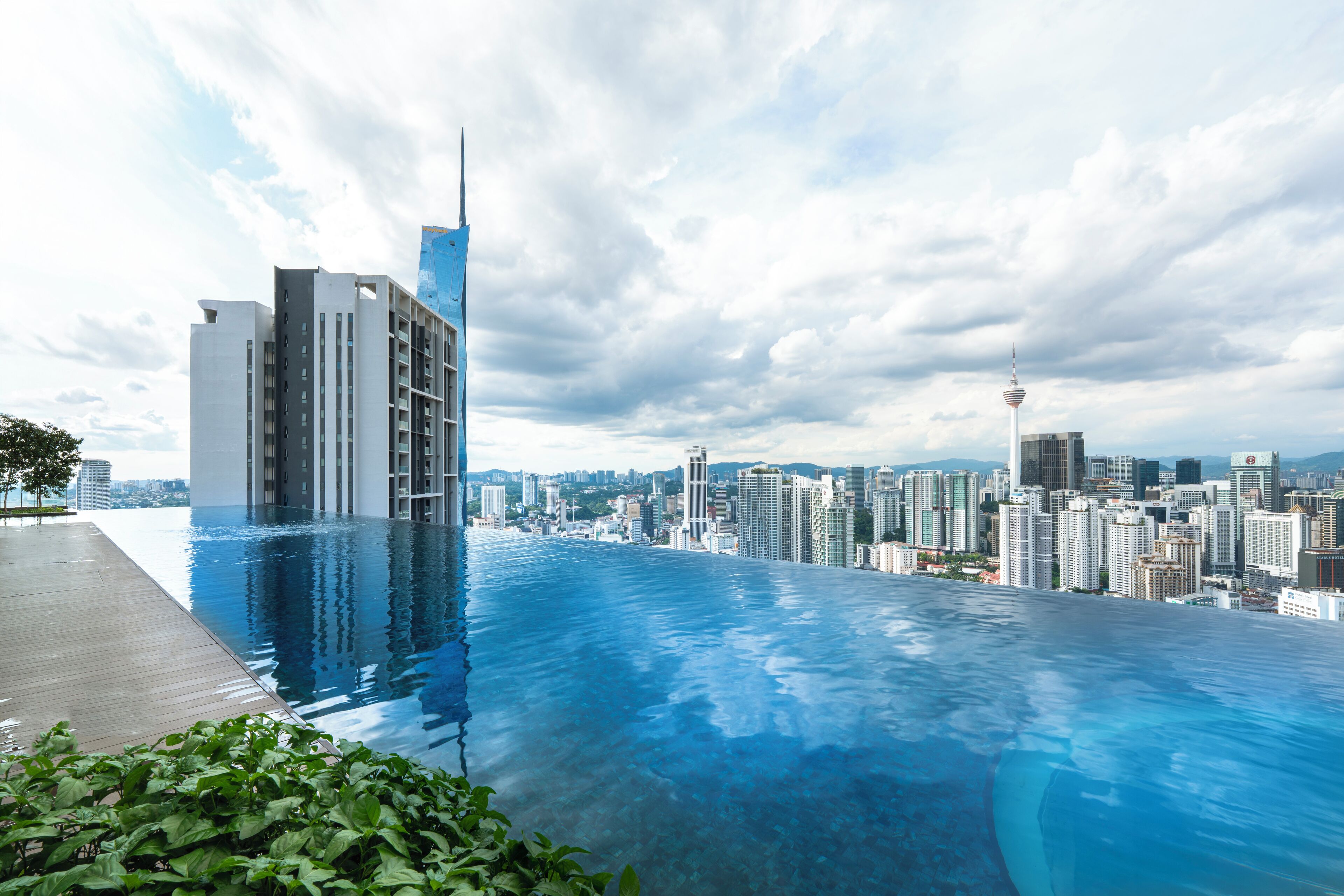Un hotel moderno con piscina infinita en la azotea y vistas a un paisaje urbano.