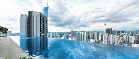 A modern hotel with a rooftop infinity pool overlooking a cityscape.